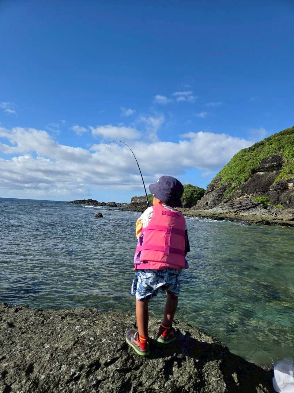 石垣島 ライフジャケットを着て岩場で釣りをする少年の後ろ姿|浜ちゃんの島遊び